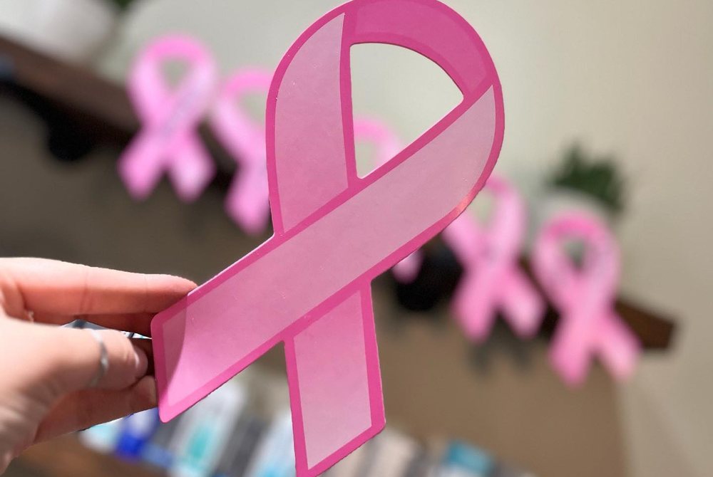 A paper pink ribbon held up in front of a shelf of pink ribbons at the salon.