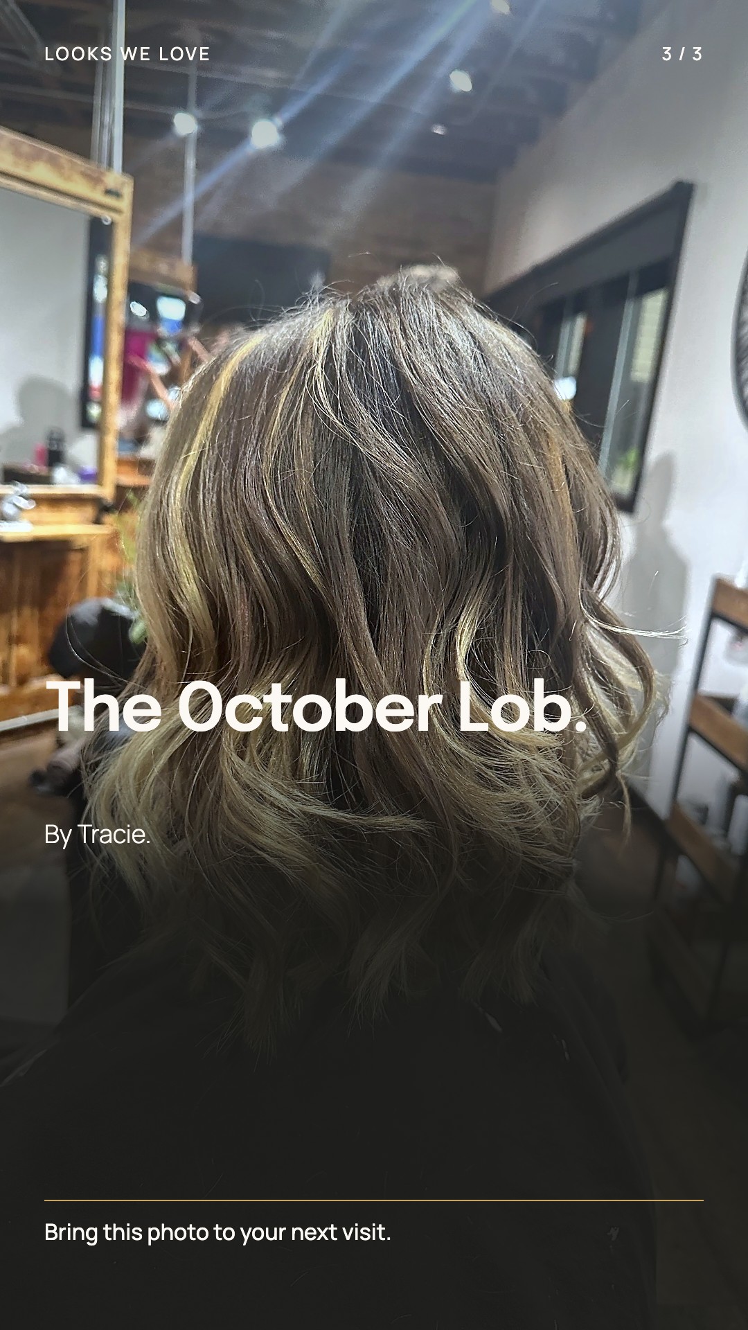Back view of Tracie's guest at the chair: shoulder-length waves with blonde pieces through brown, the wall clock and wooden mirrors around her.